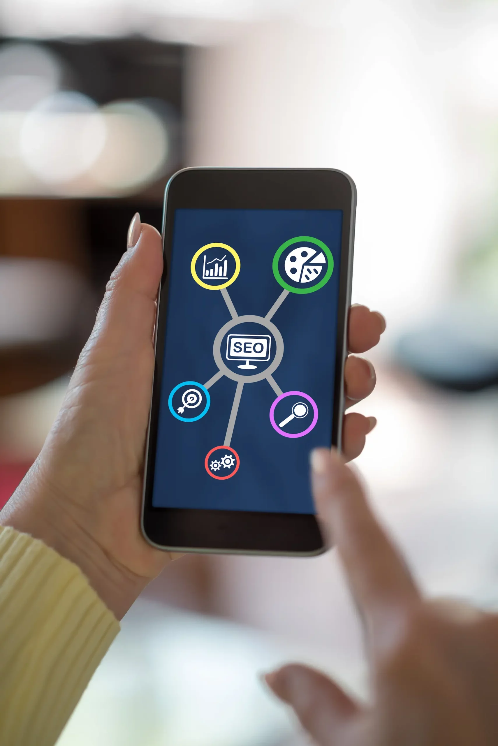 ADOBESTOCK_570185928 SCALED | Cekome Main tenant un smartphone affichant une interface SEO avec des icônes de statistiques, couleurs, recherche et paramètres