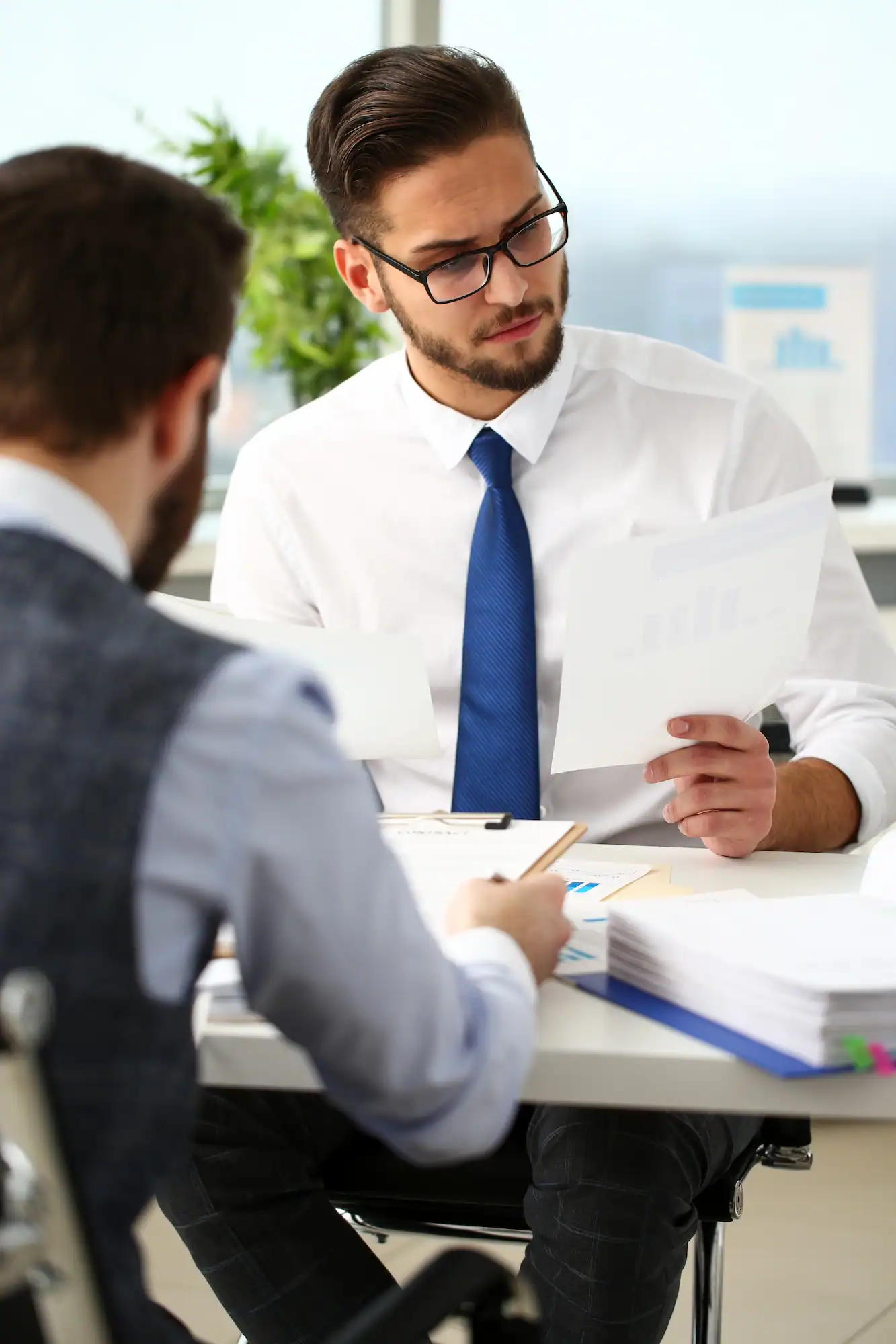 ADOBESTOCK_388817483 | Cekome Deux hommes en réunion examinant des documents sur une table de travail.