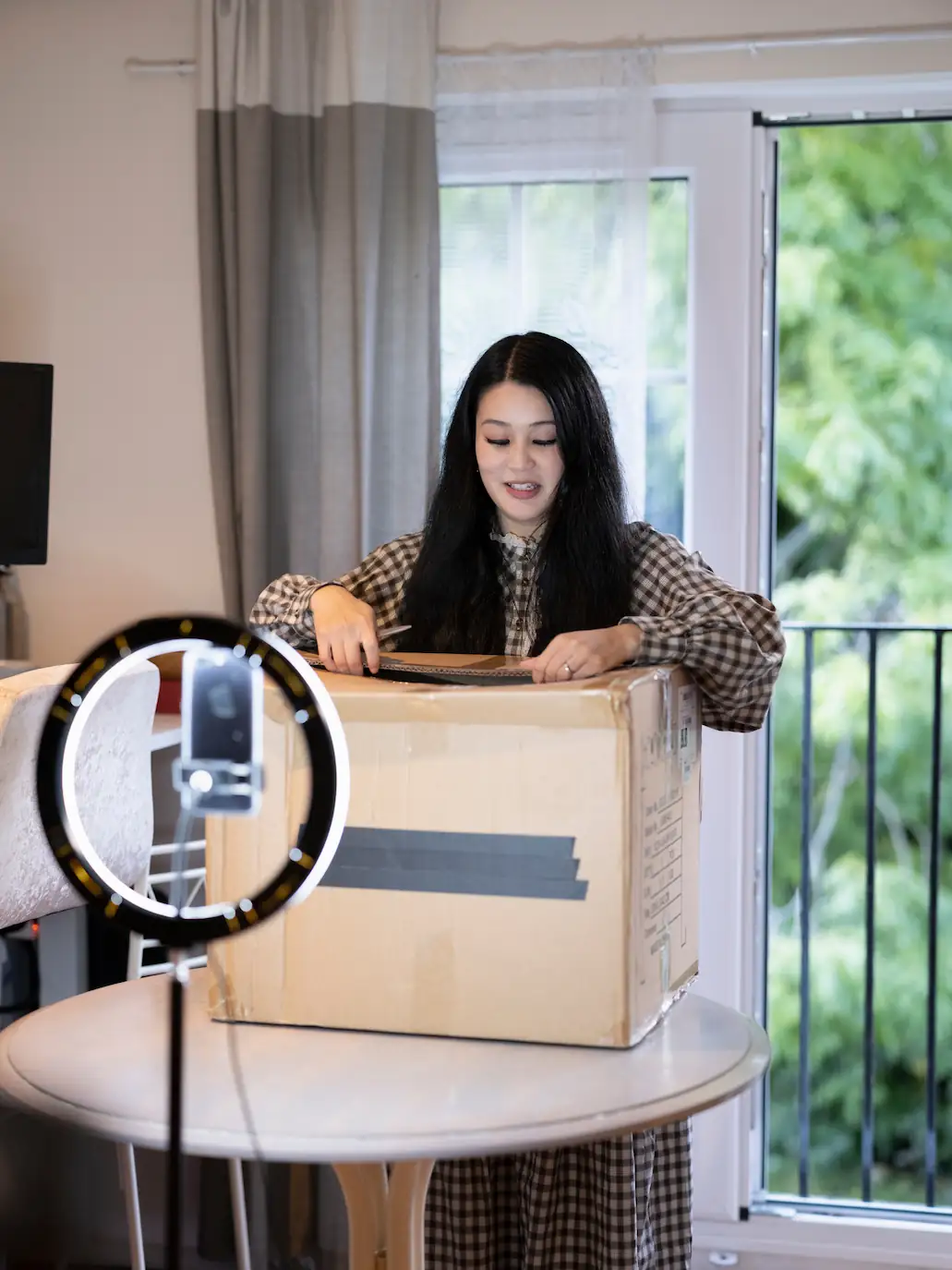 ADOBESTOCK_544953396 | Cekome Créatrice de contenu filmant un unboxing d’un colis sur une table avec éclairage en anneau.