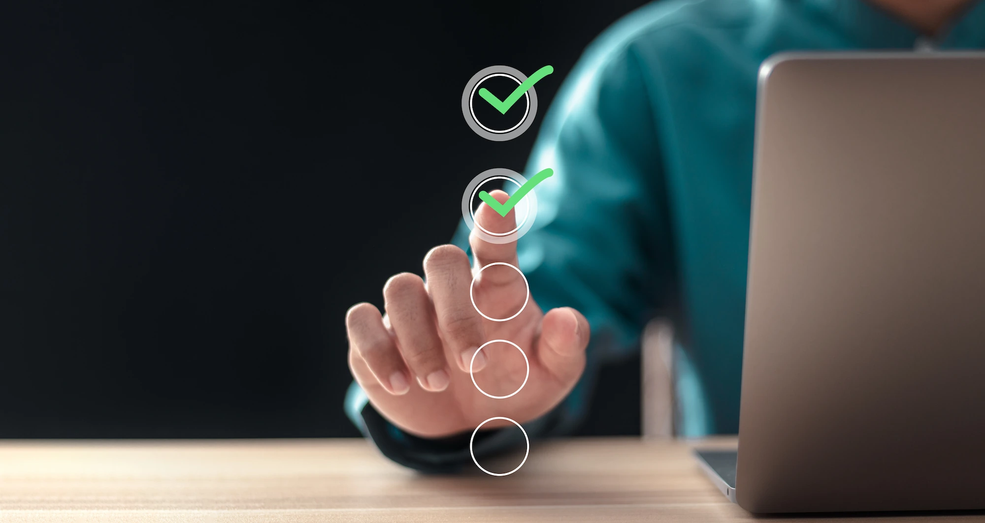 ADOBESTOCK_696386385 | Cekome Main sélectionnant une option avec une coche verte dans une interface numérique près d'un ordinateur portable.