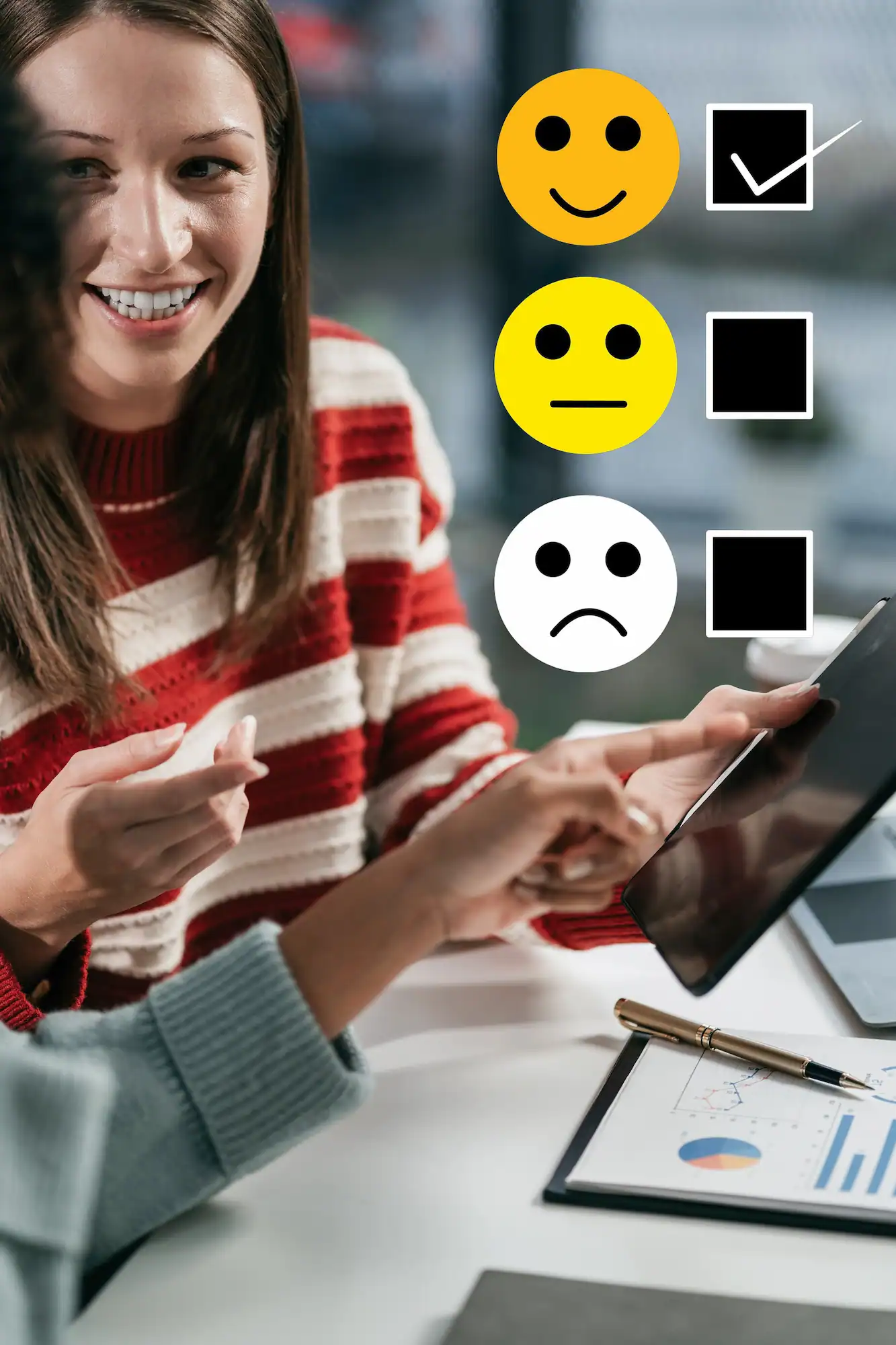 ADOBESTOCK_722120778 | Cekome Femme souriante discutant avec une autre personne, sélectionnant une option positive sur une tablette avec des émojis de satisfaction.