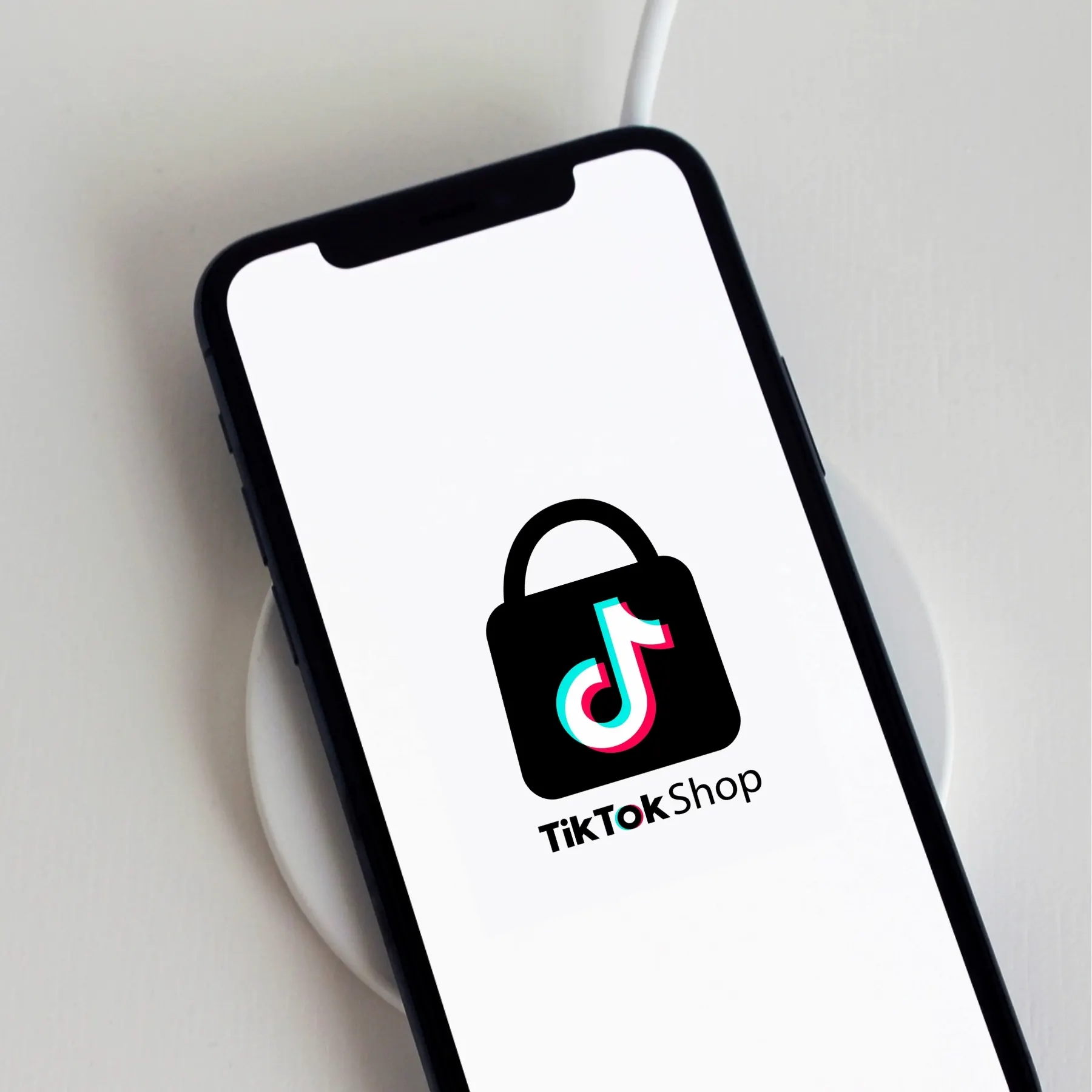 Smartphone affichant le logo TikTok Shop sur écran blanc, posé sur un chargeur sans fil.