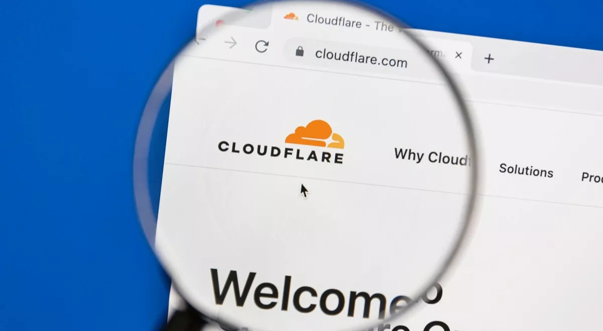 Page web de Cloudflare affichée sous une loupe, illustrant la cybersécurité et les services web