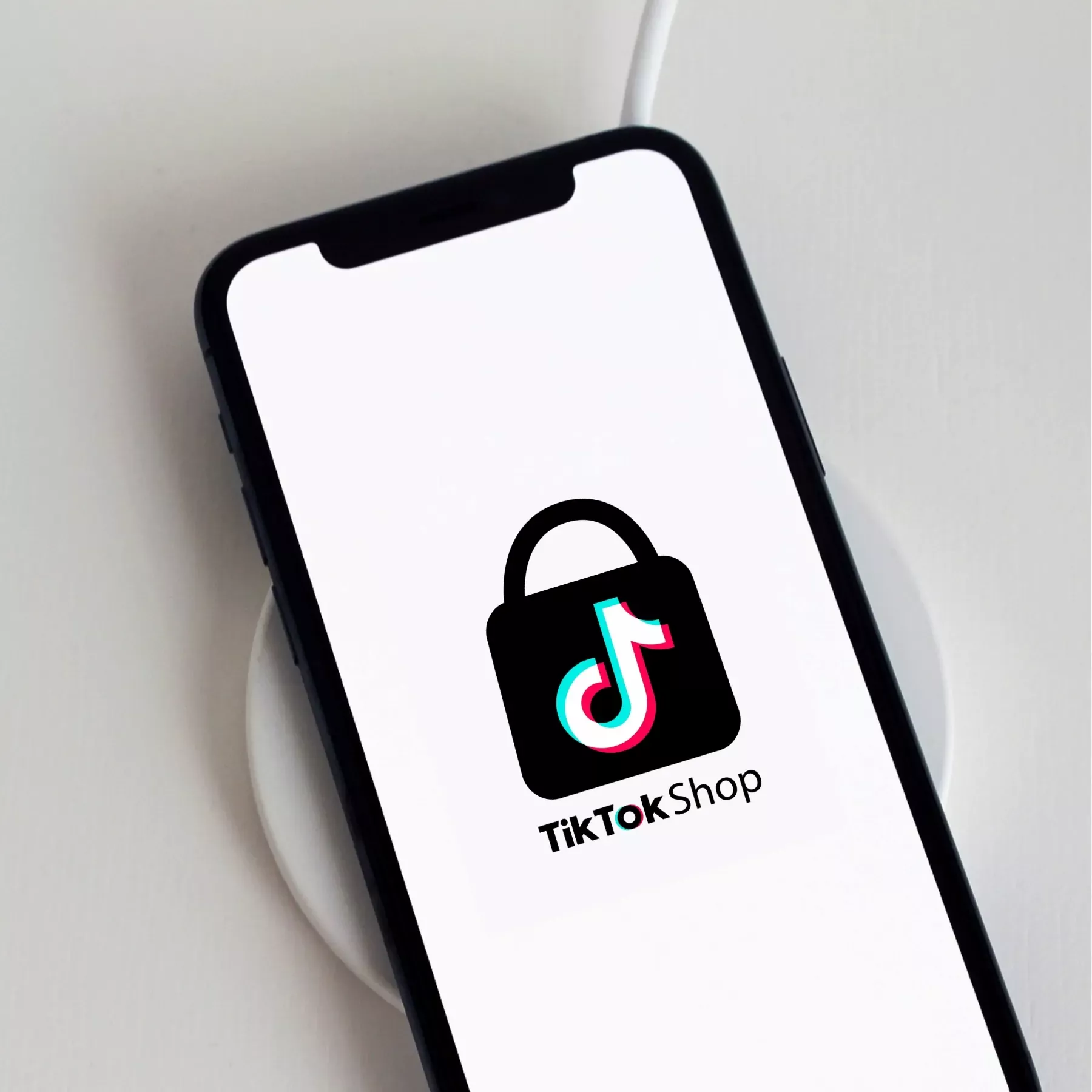 Smartphone affichant le logo TikTok Shop sur écran blanc, posé sur un chargeur sans fil.