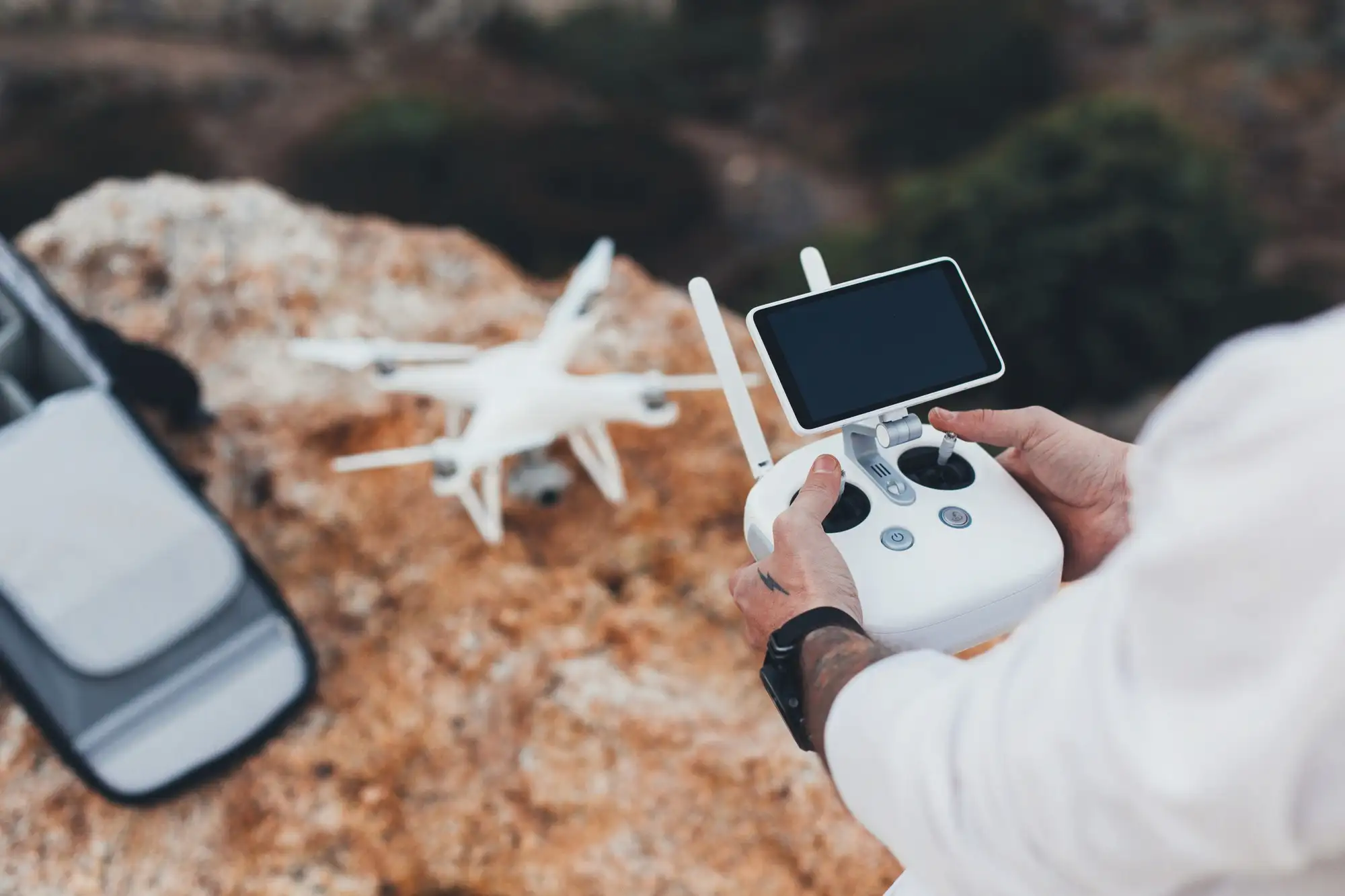 260 | Cekome Personne tenant une télécommande de drone avec écran, prêt à piloter un drone blanc posé au sol sur un terrain rocheux
