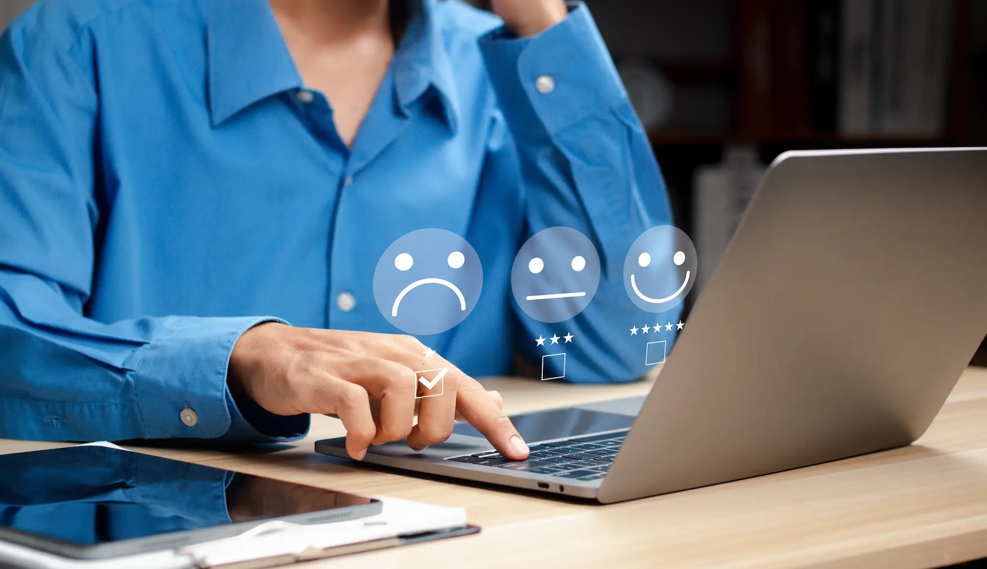 ADOBESTOCK_580206814 | Cekome Personne en chemise bleue utilisant un ordinateur portable pour évaluer un service avec des icônes de satisfaction client représentant différentes émotions.