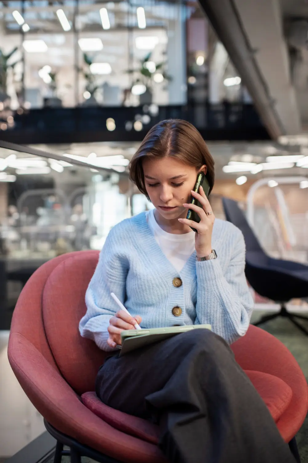 Jeune femme concentrée travaillant sur une tablette numérique tout en parlant au téléphone dans un espace de coworking moderne