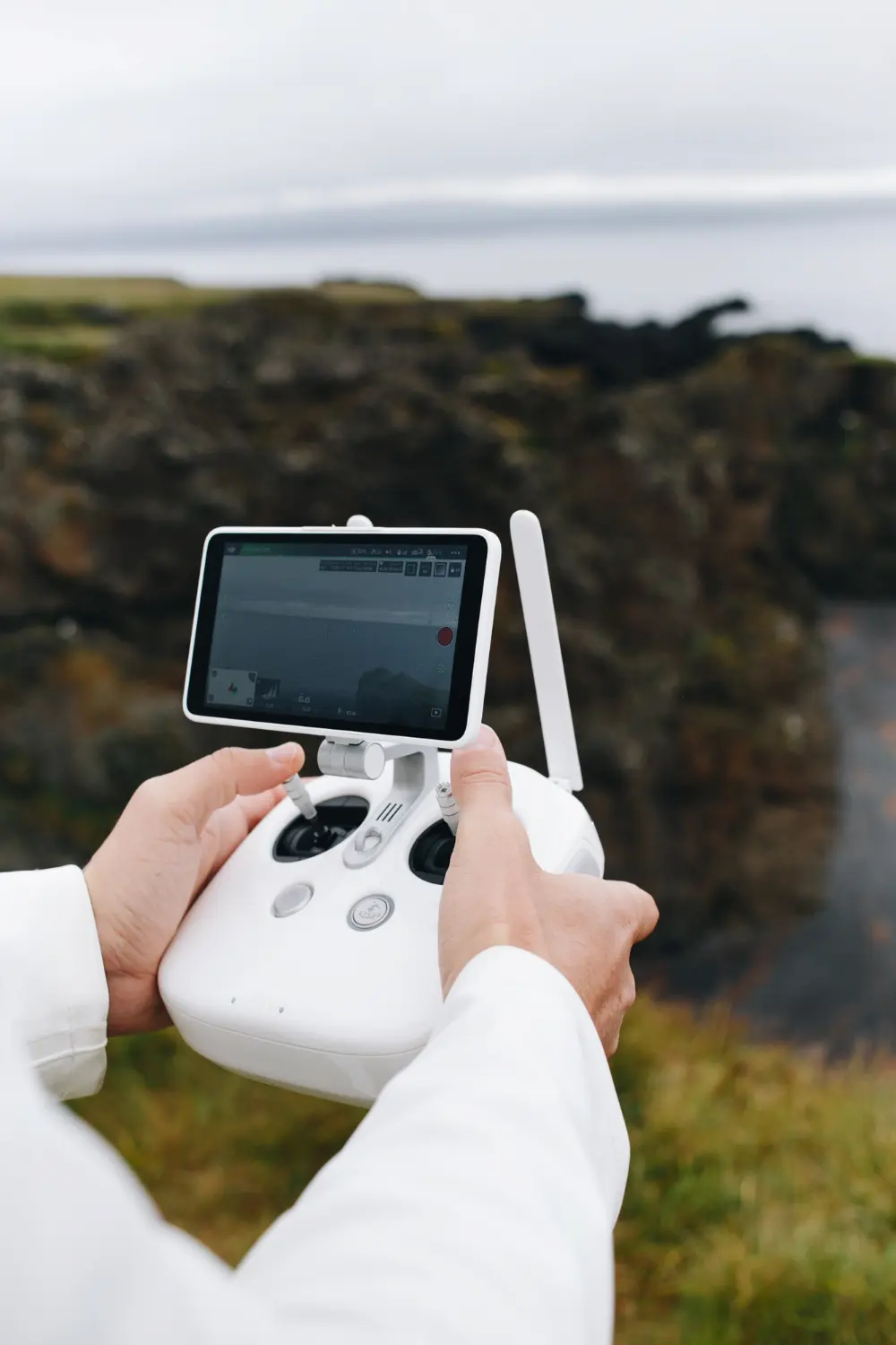 Gros plan sur les mains d’une personne manipulant une télécommande de drone avec écran intégré, en pleine nature face à un paysage rocheux