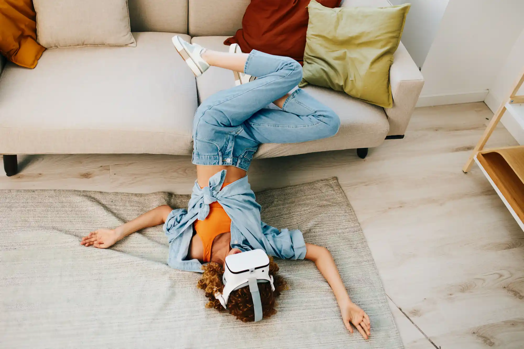ADOBESTOCK_1254382831 | Cekome Femme allongée au sol les jambes sur un canapé, portant un casque de réalité virtuelle dans un salon lumineux