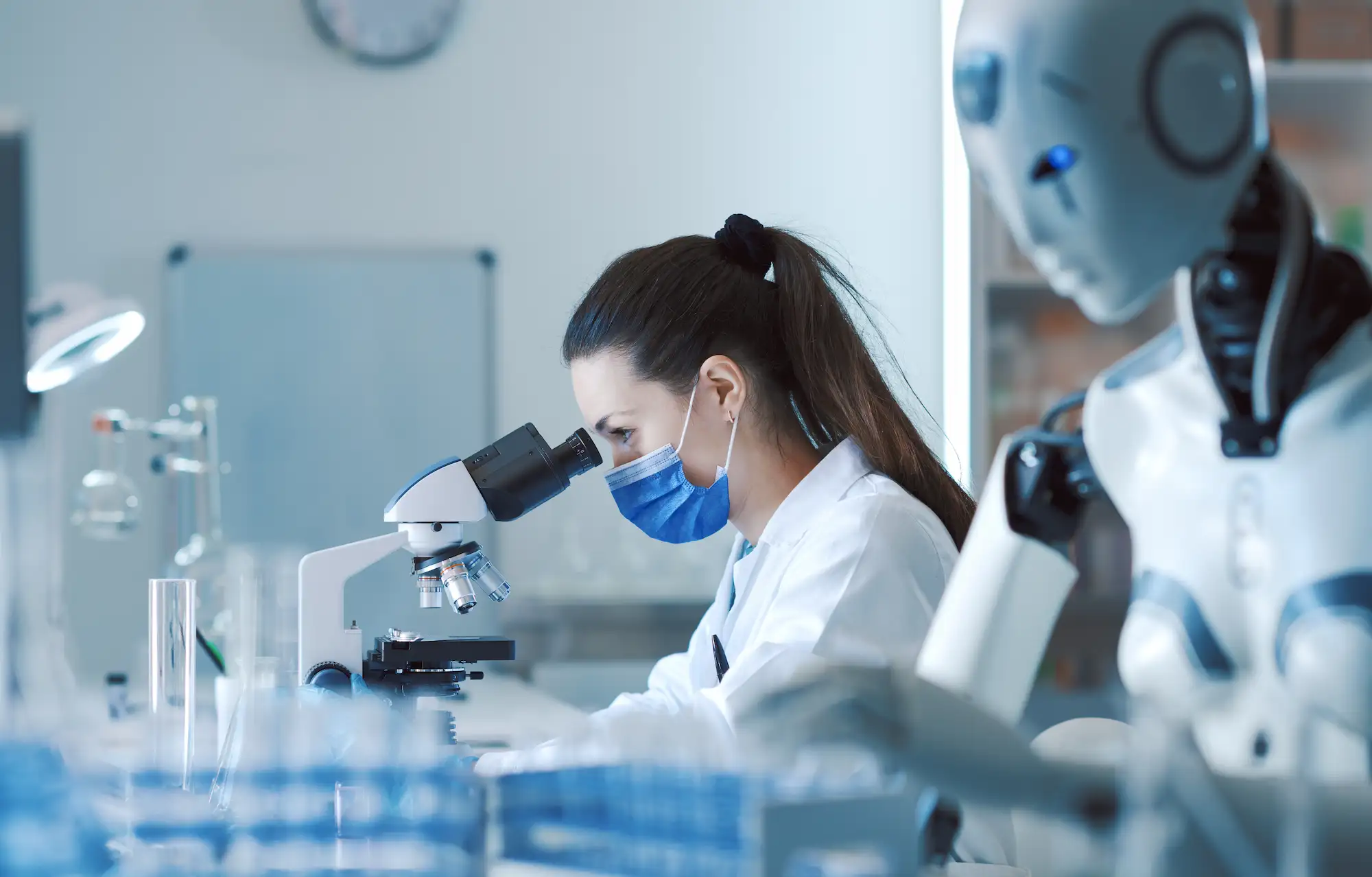 ADOBESTOCK_610936841 | Cekome Chercheuse observant au microscope dans un laboratoire avec un robot humanoïde à ses côtés