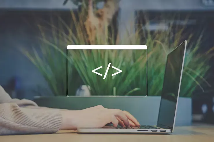 Main tapant sur un ordinateur portable avec une icône de balise HTML superposée, sur fond de plante verte