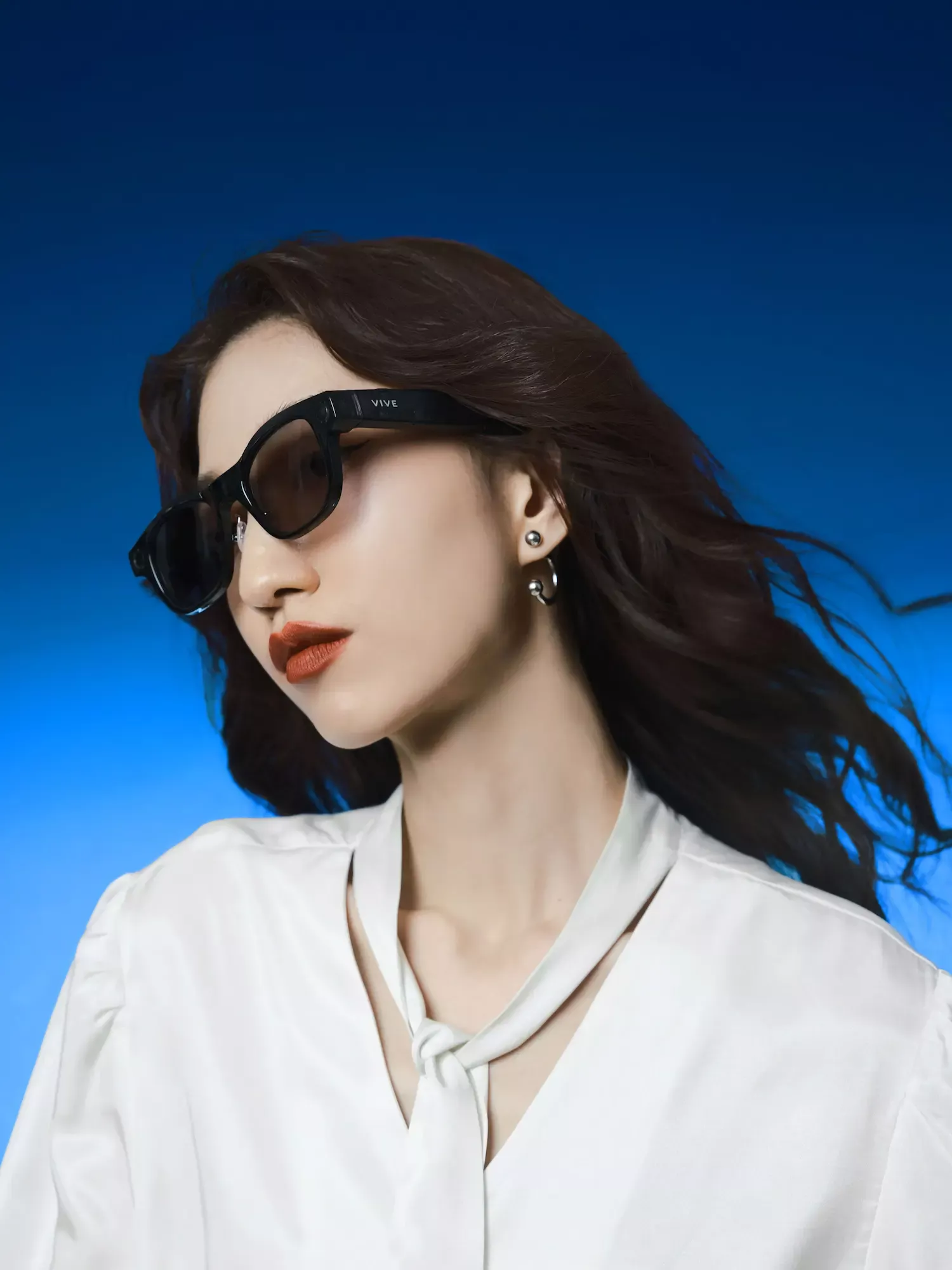 Femme portant des lunettes intelligentes VIVE noires avec un fond dégradé bleu moderne