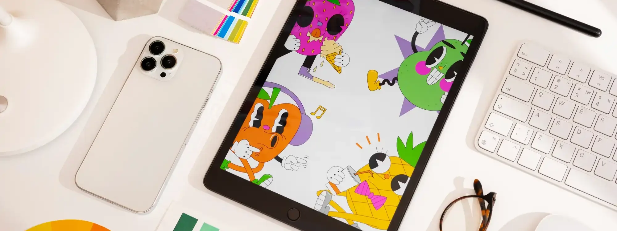 Tablette affichant des illustrations color&eacute;es pos&eacute;e sur un bureau avec nuancier, smartphone, lunettes, clavier, plante et accessoires de design graphique