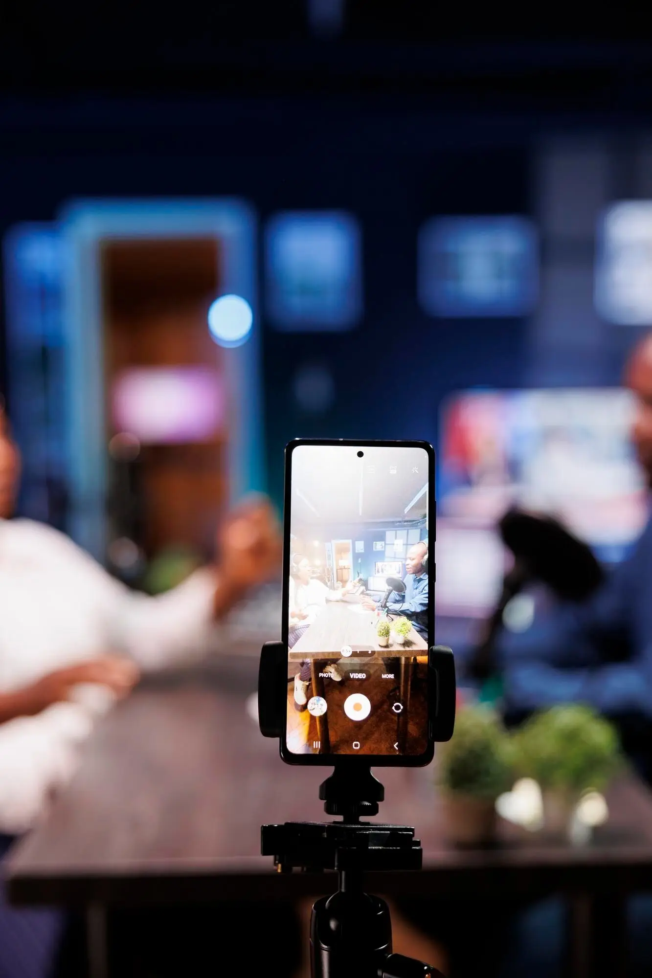 Personnes enregistrant une vid&eacute;o avec un smartphone mont&eacute; sur tr&eacute;pied dans un studio, ambiance de podcast ou interview en cours