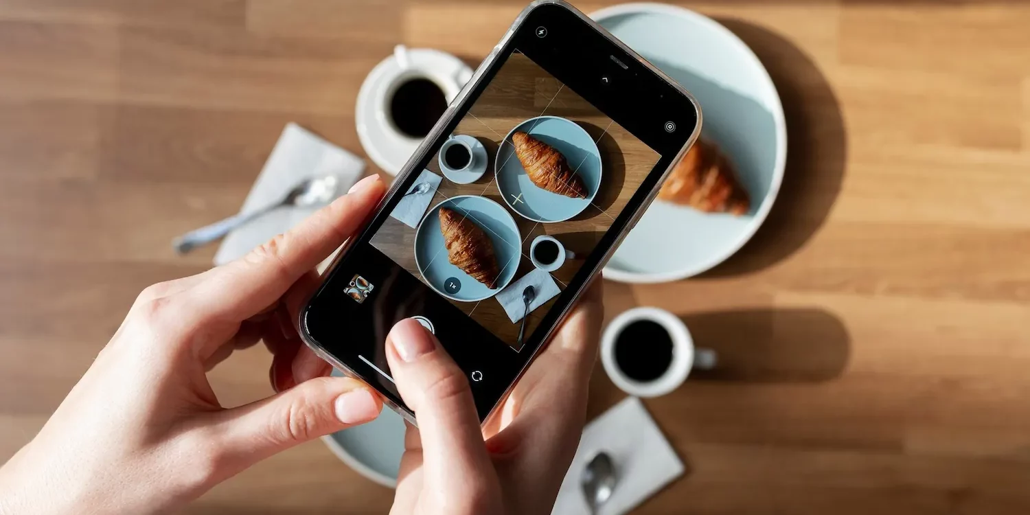 WOMAN TAKING PHOTO TWO CROISSANTS_23 2149277917 1500X750 | Cekome Personne prenant une photo de croissants et café avec un smartphone pour un post Instagram culinaire
