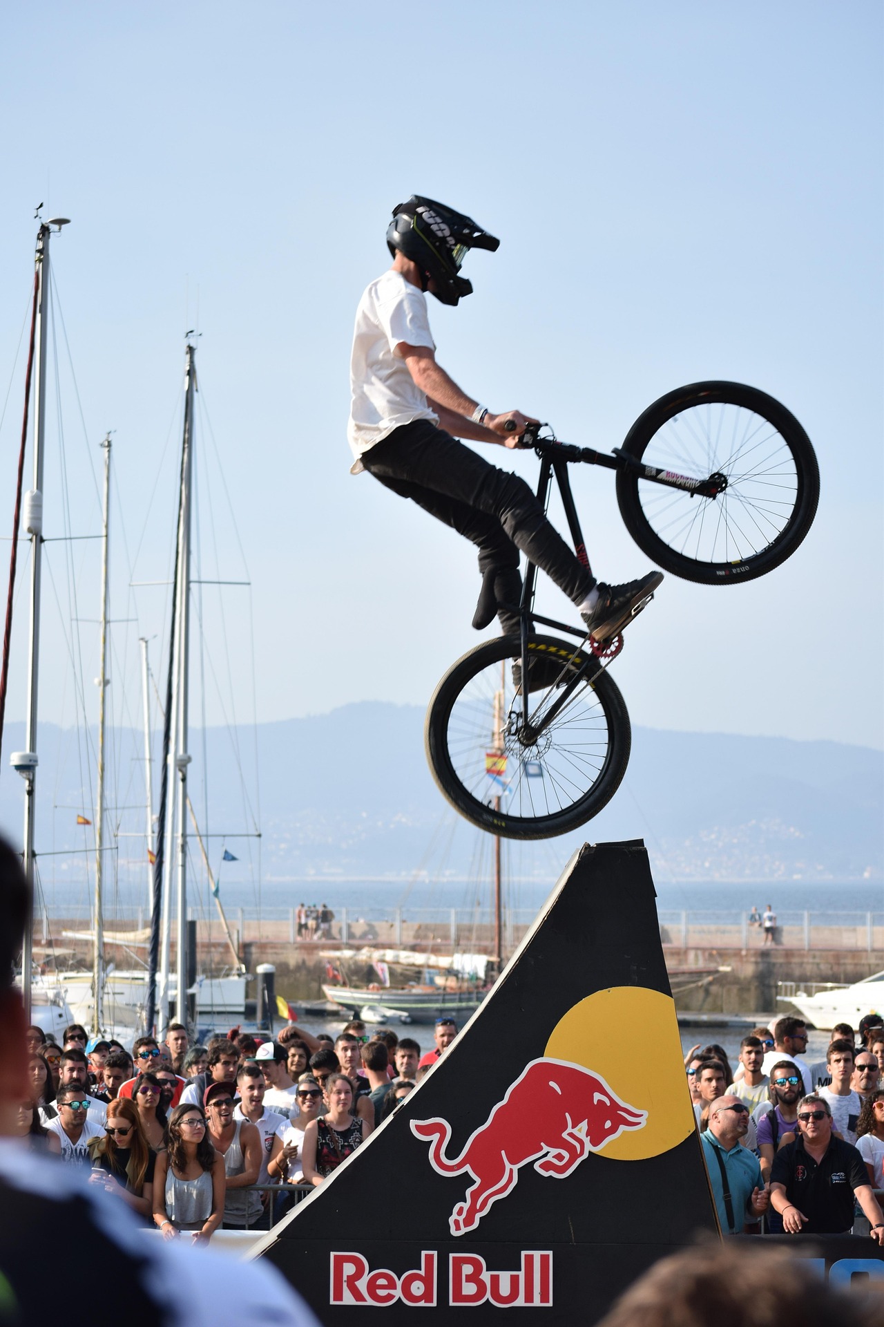 Biker effectuant une figure acrobatique sur une rampe Red Bull devant une foule en plein air pr&egrave;s du port