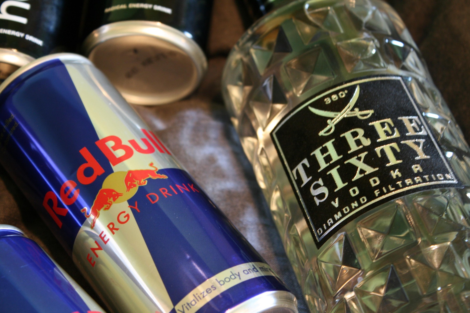 Canette de Red Bull pos&eacute;e &agrave; c&ocirc;t&eacute; d'une bouteille de vodka Three Sixty sur un tissu sombre