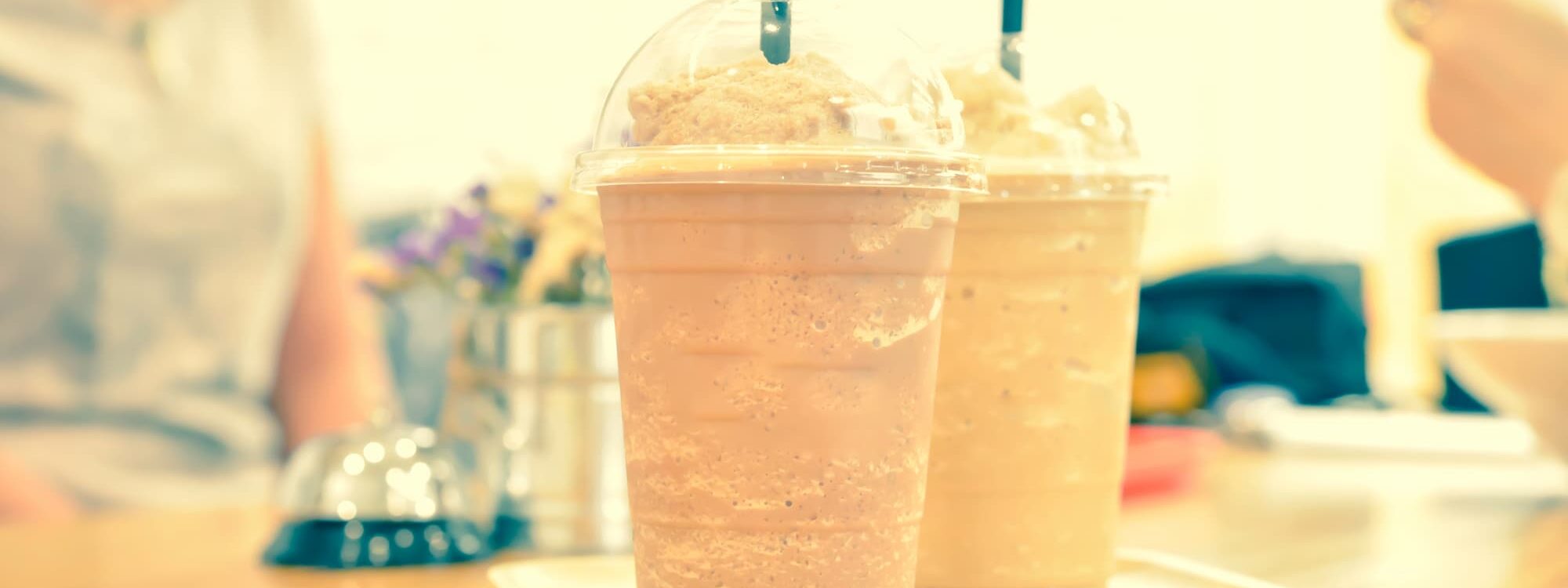 DEUX CAFES FRAPPES DANS DES GOBELETS EN PLASTIQUE AVEC PAILLES POSES SUR UN PLATEAU EN BOIS DANS UN CAFE 2000X750 | Cekome Deux cafés frappés dans des gobelets en plastique avec pailles, posés sur un plateau en bois dans un café