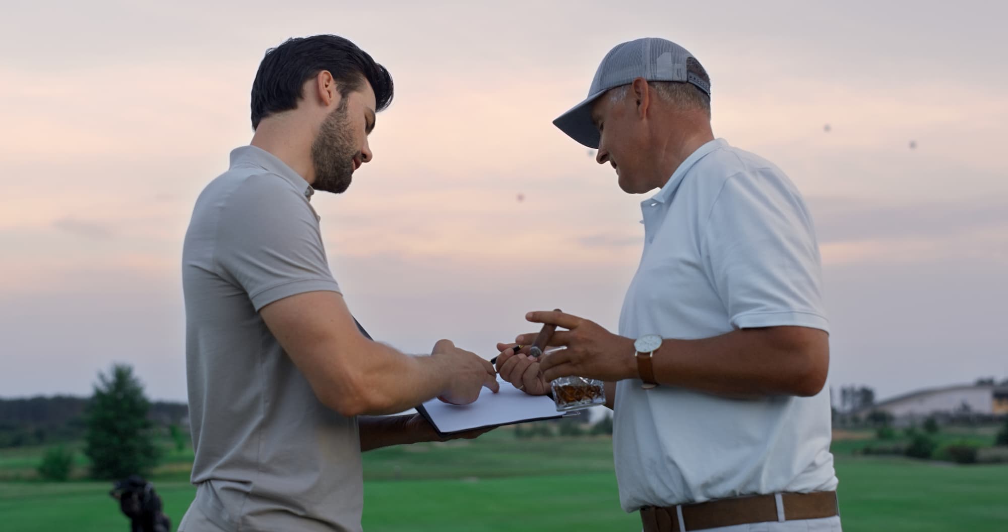 DEUX HOMMES DISCUTANT SUR UN TERRAIN DE GOLF AU COUCHER DU SOLEIL | Cekome Deux hommes discutant sur un terrain de golf au coucher du soleil.