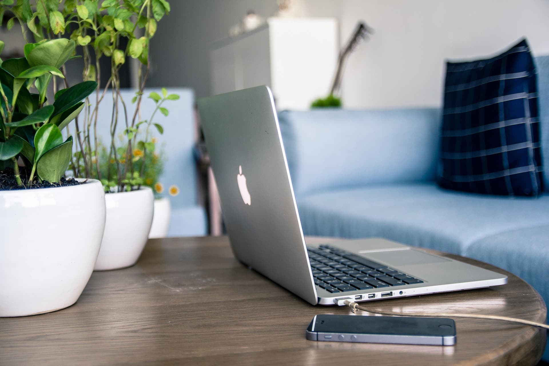 MACBOOK ET IPHONE POSES SUR UNE TABLE DANS UN SALON AVEC PLANTES EN POT | Cekome MacBook et iPhone posés sur une table dans un salon avec plantes en pot