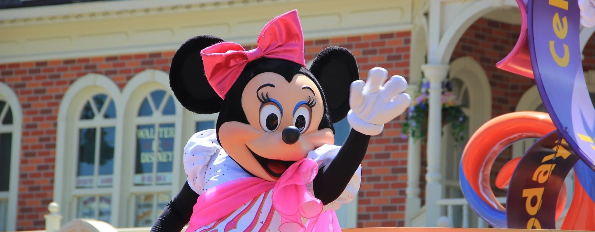 MINNIE MOUSE EN ROBE ROSE SALUANT LORS DUNE PARADE DISNEY DEVANT UN BATIMENT VICTORIEN 1920X750 | Cekome Minnie Mouse en robe rose saluant lors d'une parade Disney devant un bâtiment victorien