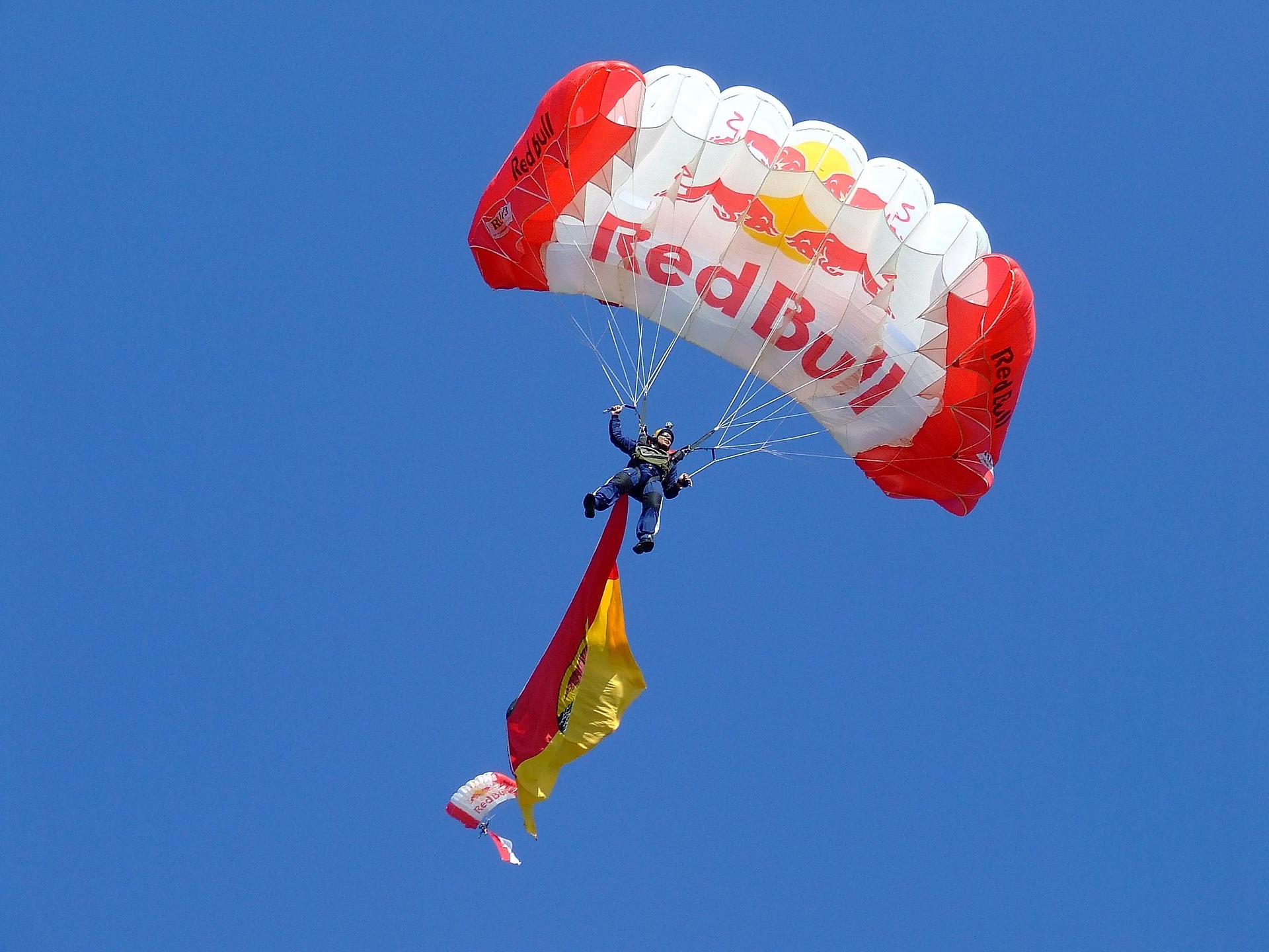 Parachutiste avec une voile Red Bull d&eacute;ployant un drapeau color&eacute; dans le ciel bleu
