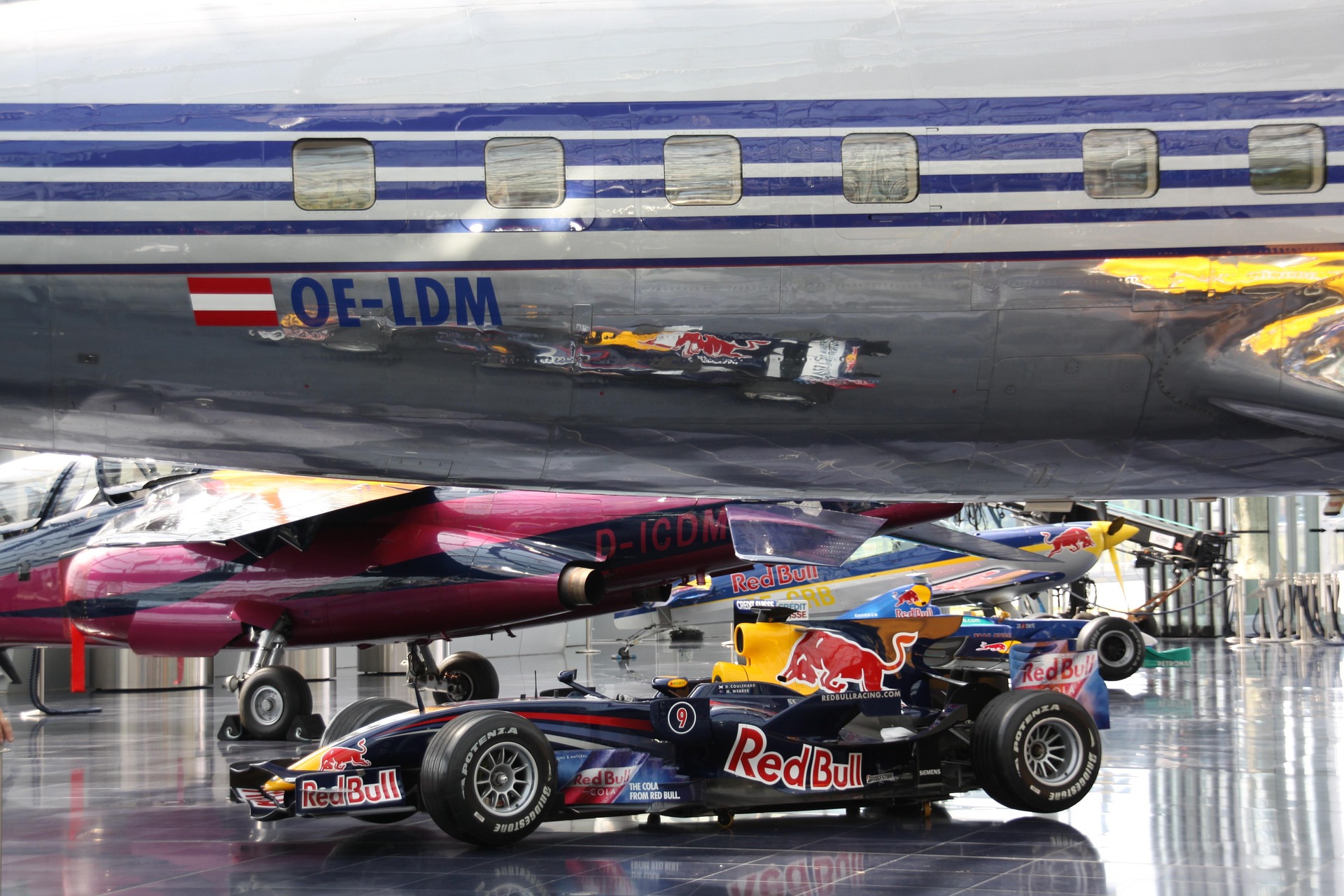 Voiture de Formule 1 Red Bull expos&eacute;e sous un avion dans un hangar moderne