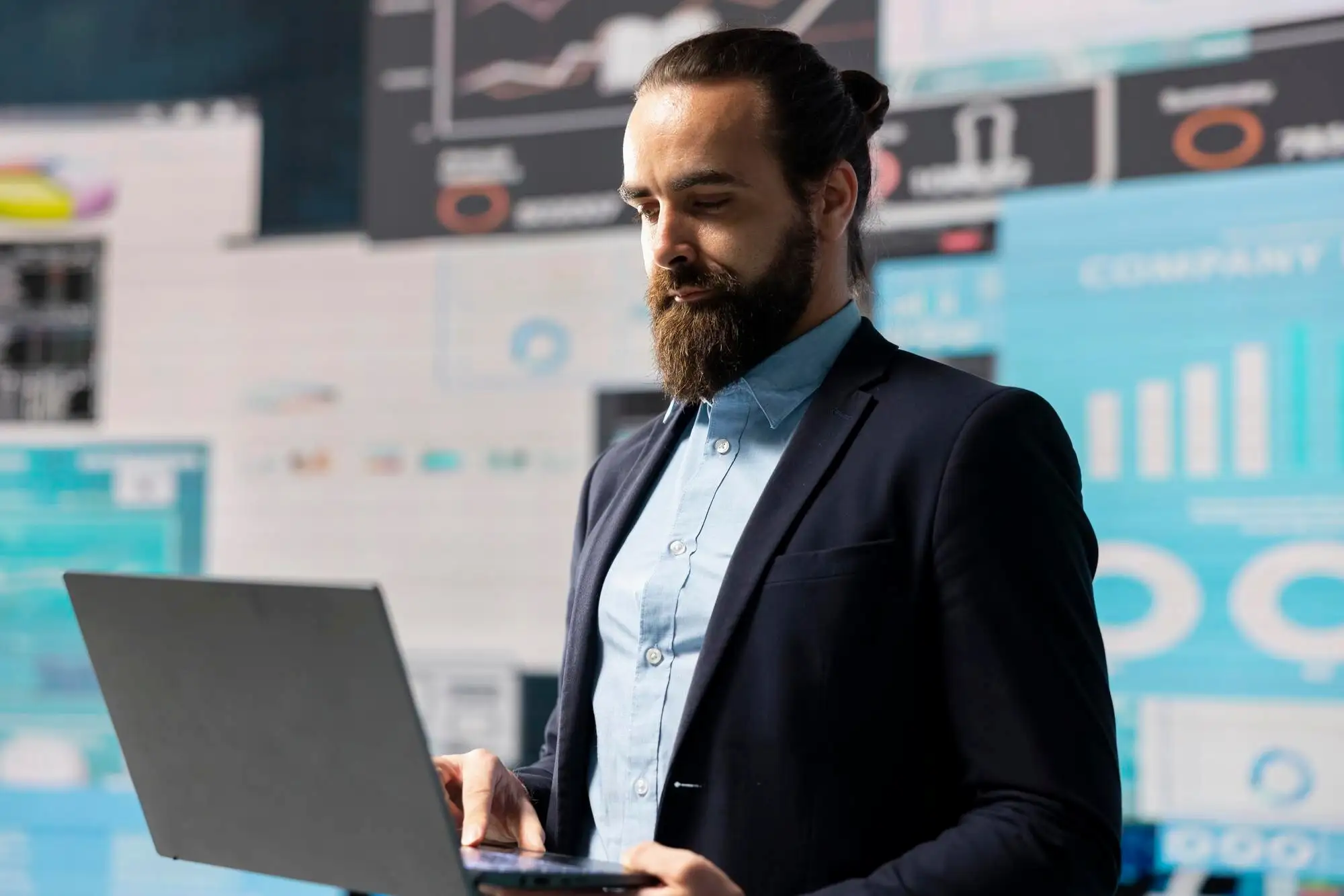 DATA DRIVEN PLANNING HELPS THIS PROFESSIONAL BUILD SUCCESSFUL STRATEGY_482257 126336 | Cekome Homme en costume consultant des données sur un ordinateur portable devant un mur d’écrans d’analyse numérique