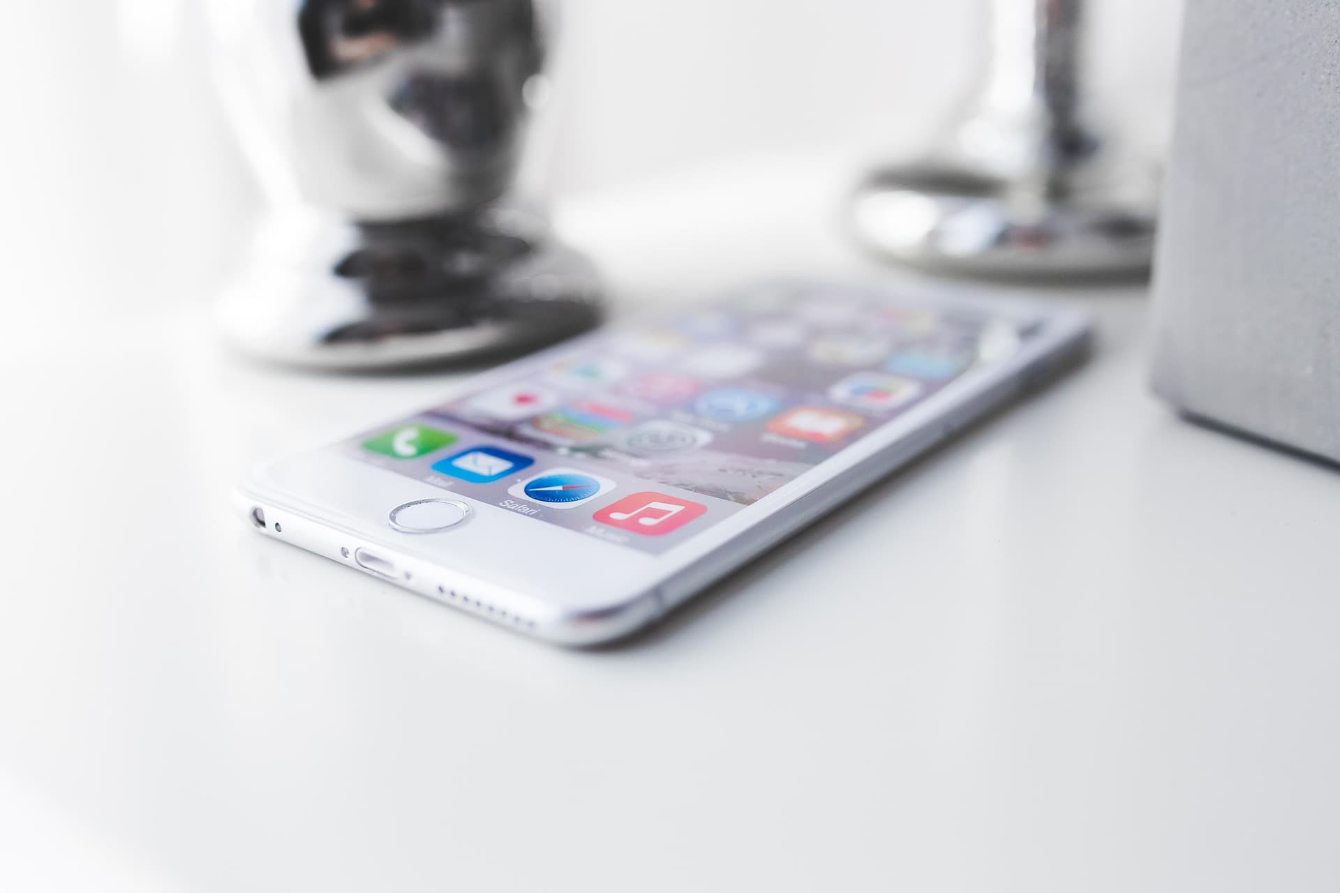 PHONE 762550_1920 1 | Cekome iPhone argenté posé sur une surface blanche, affichant l'écran d'accueil avec plusieurs applications